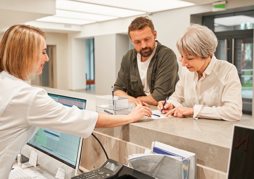 A receptionist checking in two patients at a dental clinic desk